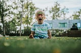 A young boy sitting in the grass and screaming with his mouth open.