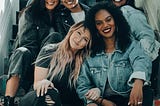 A group of seven women of different races and ethnicities sitting and smiling,  sitting on some steps.