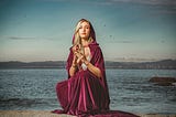 A mystic sits on a beach holding a crystal ball