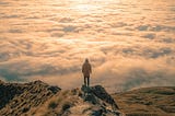 man standing on moutaintop, looking down at clouds.