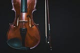 Partial photo of a violin and bow on a black background.