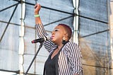 image of a black woman speaking at a microphone with her arm raised in the air