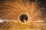 A spray of light spins out from a central circle, behind which is a city scape at night.