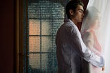 man hugging woman behind sheer curtain