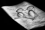 Black and white image of wire-framed glasses on a folded newspaper.