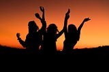 three women dancing in with an orange sky in the background