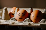 Two eggs in an egg box, anthropomorphised with sad faces