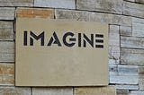 black text with the word imagine on a piece of slate, on a slate wall.