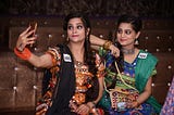 Indian twins smiling Garba dancer women taking selfie on smartphone at Dandiya night on the occasion of Navaratri Dussehra, with the number tags.