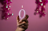 Girl’s hand holding a lit candle shaped as a zero with glittery shapes in the background