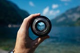 a hand holding up an object to zoom in on a water and mountain view