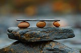 Flat stone balanced on three round stones on a larger stone balanced on a boulder.