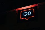 pink neon sign in a black background featuring a facebook notification of zero likes