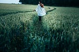 A woman walks along a path of deep grass.