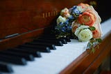 Old style piano, with a bunch of flowers on the keyboard.