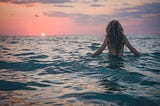 woman standing in ocean watching the sun set