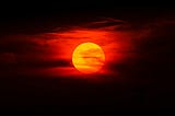 A picture of a red moon, most likely the blood moon, against the backdrop of a back sky; signifies the light-dark crossroad of endings and new beginnings.