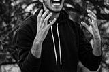 A young man passionately expresses anger or frustration, gesturing dramatically against a blurred natural background