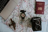 A photo array of pre-digial travel items, including a map, a camera and a compass.