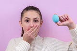 Surprised brunette girl stands on a pink background and holds an Easter egg. Easter. Easter bunny. Easter egg. Holiday. Advertising. Place for an inscription. Postcard. Brunette girl. Smirk