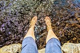 Someone sitting on a rock, dipping their feet in the river below