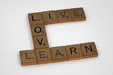 Brown wooden squares with black capital letters on them and a small number, one on each square, arranged to say “Live, Love, Learn”