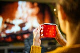 A woman drinking from a red cup in front of a fireplace. Cancelation of Stephen Colbert, The Late Show Stephen Colbert, Strike Force Five, Entertainment, Myers, Stewart, Late Night, Kimmel, talk show, comedy, first amendment, when is late show ending? Oliver, Fallon, democracy, mental health, coffee, Paramount, CBS, opinion, stress, mental decline, sucking taxpayers, Colbert last show.