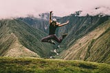 Photo of a person jumping in the air, appearing joyous against a background of rolling hills.