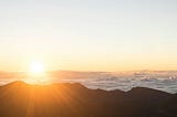 A landscape with the sun rising against a light blue sky..