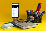 A notebook, sticky notes, pens, glasses, and an app