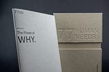 The image shows a book titled “The Power of Why”. The book is sitting on a table next to a cardboard box. The book is open to a page with the text “77 WEE PHUMAN”. The box has the text “The Power of WHY. 77HUMAN NEEDS”.
 
 The image is simple and minimalist, with a focus on the book and the text. The colors are muted, with the dominant colors being white, black, and brown. The overall impression is one of calm and introspection.