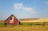 A farm with its barn displaying a large American flag.