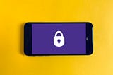 A smartphone rested on a yellow background. On the smartphone screen is a white lock icon resting on a blue background.