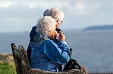 Elderly couple sitting on a bench looking out over the water.
