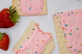 Homemade strawberry pop-tart pastries with sprinkles alongside two strawberries