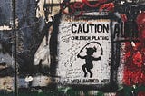 The picture shows a sign on which is a little girl jumping rope with what looks like barbed wire. The words on the image read “CAUTION, CHILDREN PLAYING.” The sign is surrounded by bold flashes of red and black in graffiti style. The image is in the style of the artist Banksy.
