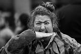 person with a mustache and long hair in bun appears to bite their own hand performatively