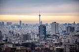 A photo centered on a tall tower in Tehran with a few high-rise buildings of perhaps 30 stories.
