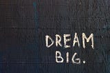 A textured wall with the words “dream big” painted on it.