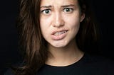 A 20-something year old Caucasian girl with brown hair, wearing a black shirt and staring straight ahead with a confused look on her face.