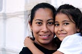 A woman smiling, holding a little girl who is smiling.