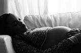 A pregnant woman laying on sofa, touching her belly.