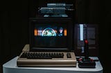 A dark room with a Commodore 64 keyboard, a small colour monitor, and a joystick.