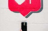 A hand holding a phone and a large red like heart.