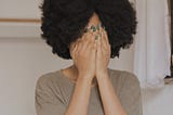 Black woman covering her face with her hands.