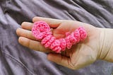 A pink crochet “worry worm” held in an open palm