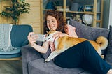 Image of woman sitting with her dog on a sofa taking a selfie.
