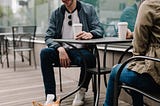 man and woman drinking coffee and looking at their pet corgi dog.