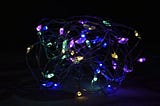 Photo of a tangled string of Christmas lights in the dark, with the small pools of of multicoloured light illuminating the wires that connect them.