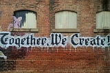 gothic script on a brick wall, reading “together we create”